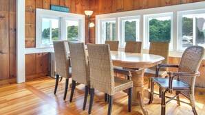 Un comedor con sillas de mimbre, una mesa de madera y grandes ventanales con vistas a zonas verdes.