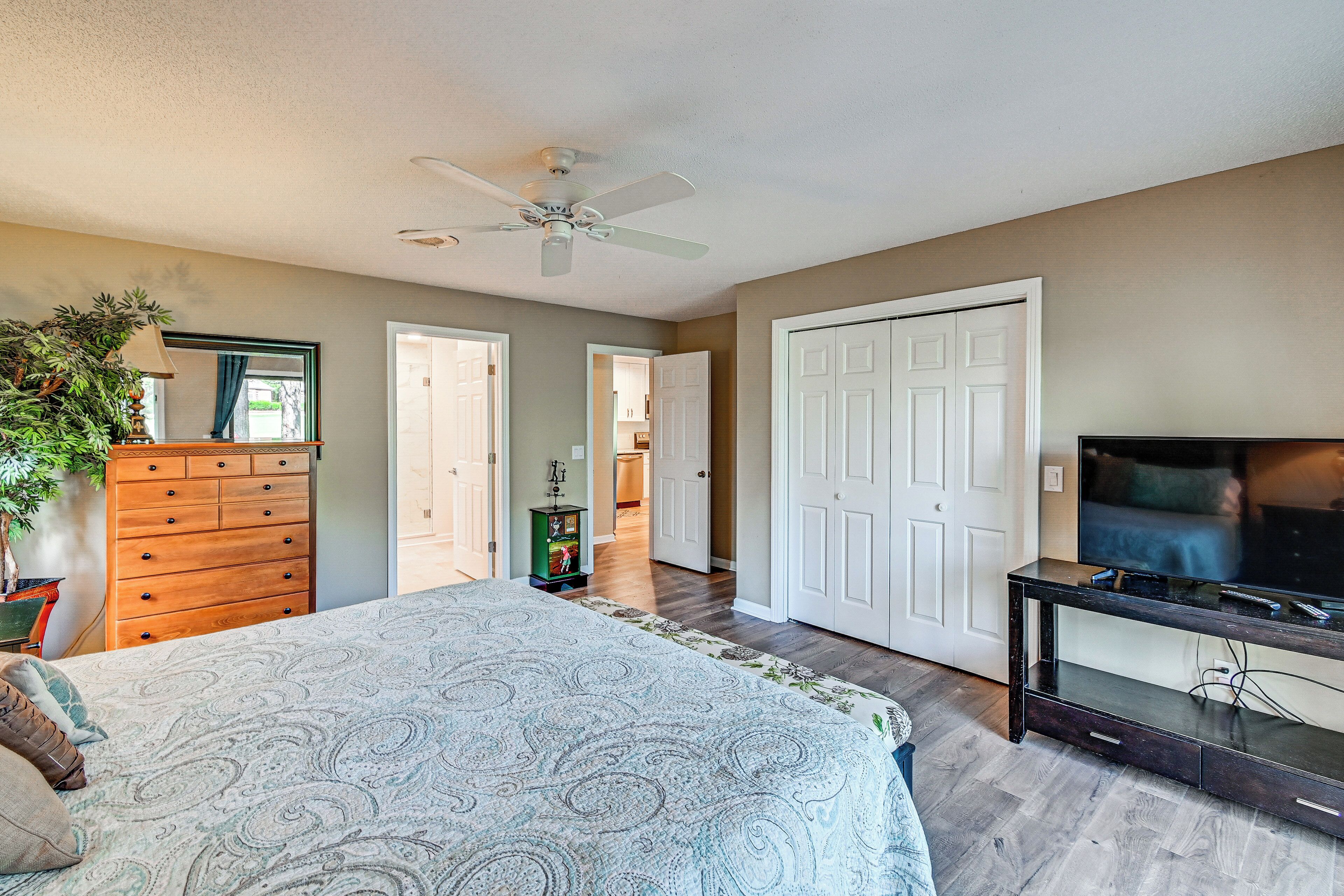 A bedroom with a bed, dresser, TV stand, and a ceiling fan.