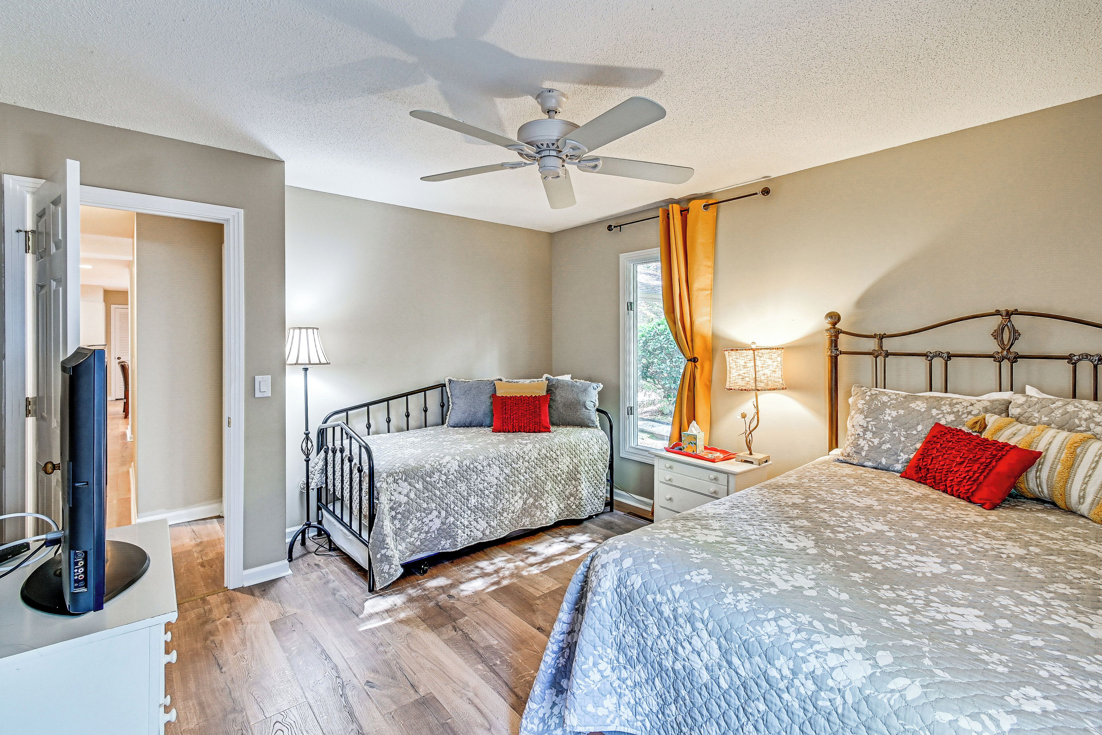 A bedroom with two beds, a ceiling fan, a TV, and a window with curtains.