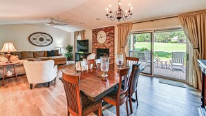 A spacious living room with a wooden dining table, comfortable seating, a fireplace, and a large window offering a view of the outdoors. - Charming Pinehurst Getaway w/ Golf Course View! (Pinehurst)