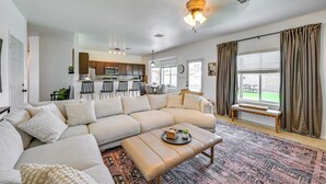 Uma sala de estar moderna com um sofá seccional, uma mesa de centro e uma área de jantar ao fundo.