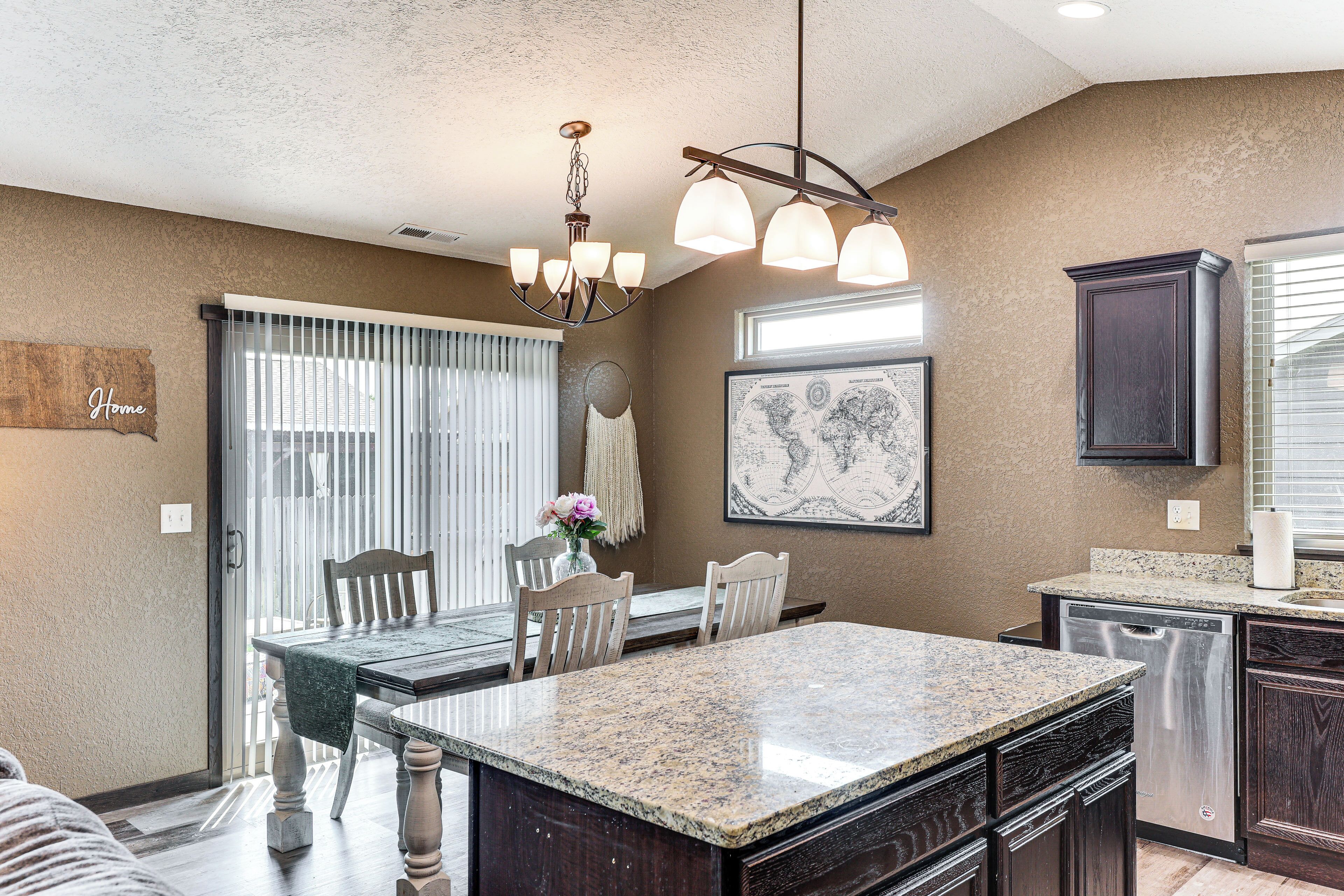 A kitchen with granite countertops, dark wooden cabinets, a built-in dishwasher, and a dining area with a table and chairs.