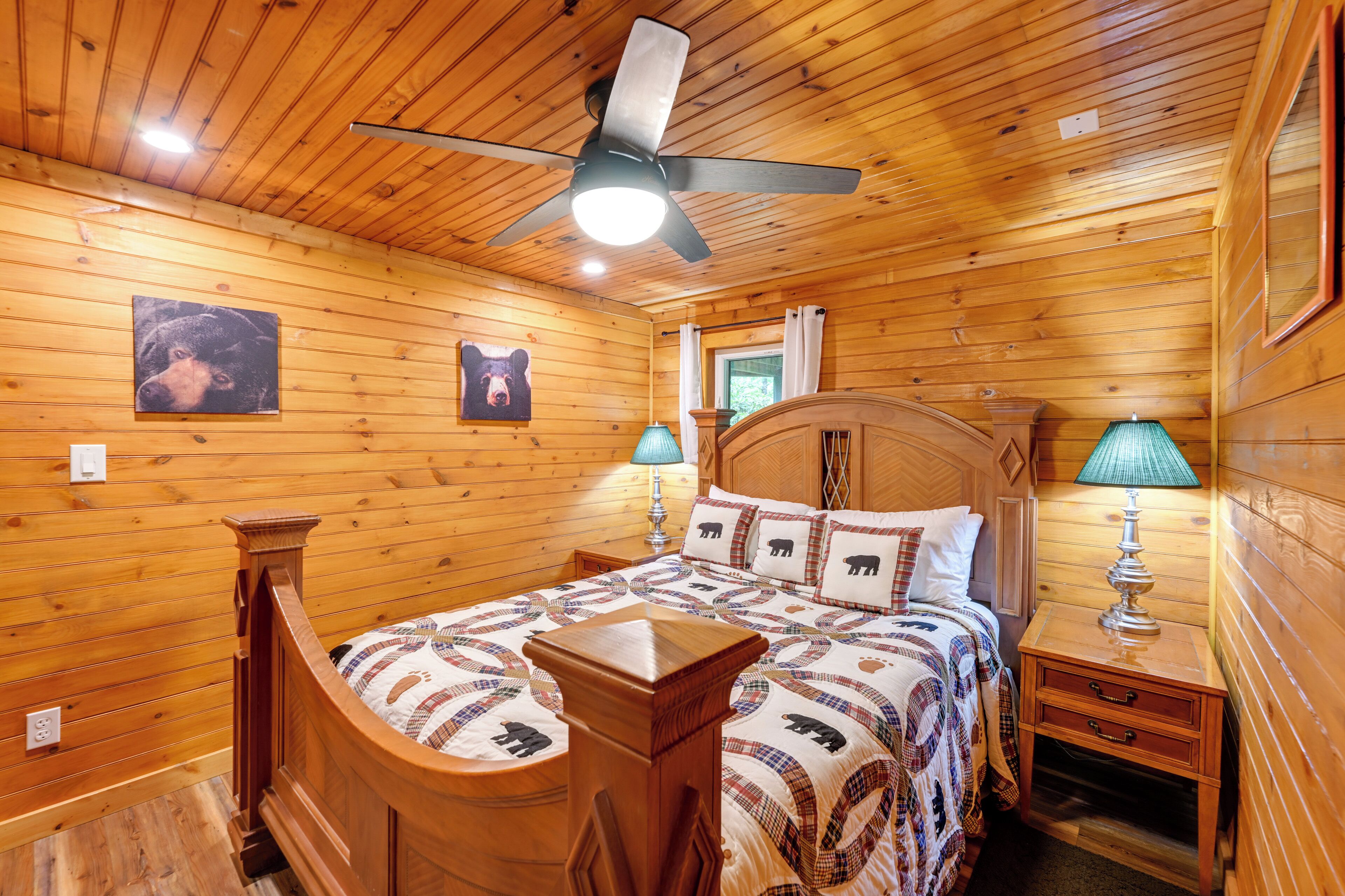 Une chambre dans une cabane en bois, avec un lit, des tables de chevet, un ventilateur de plafond et une fenêtre.
