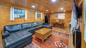A cozy cabin interior with a leather sofa, a wooden coffee table, and a dining area with wooden chairs and a table. - 6 Mi to Town: Robbinsville Apt w/ Deck & Grill (Robbinsville)