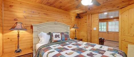 A wooden cabin bedroom with a bed, two bedside lamps, a ceiling fan, and a window.