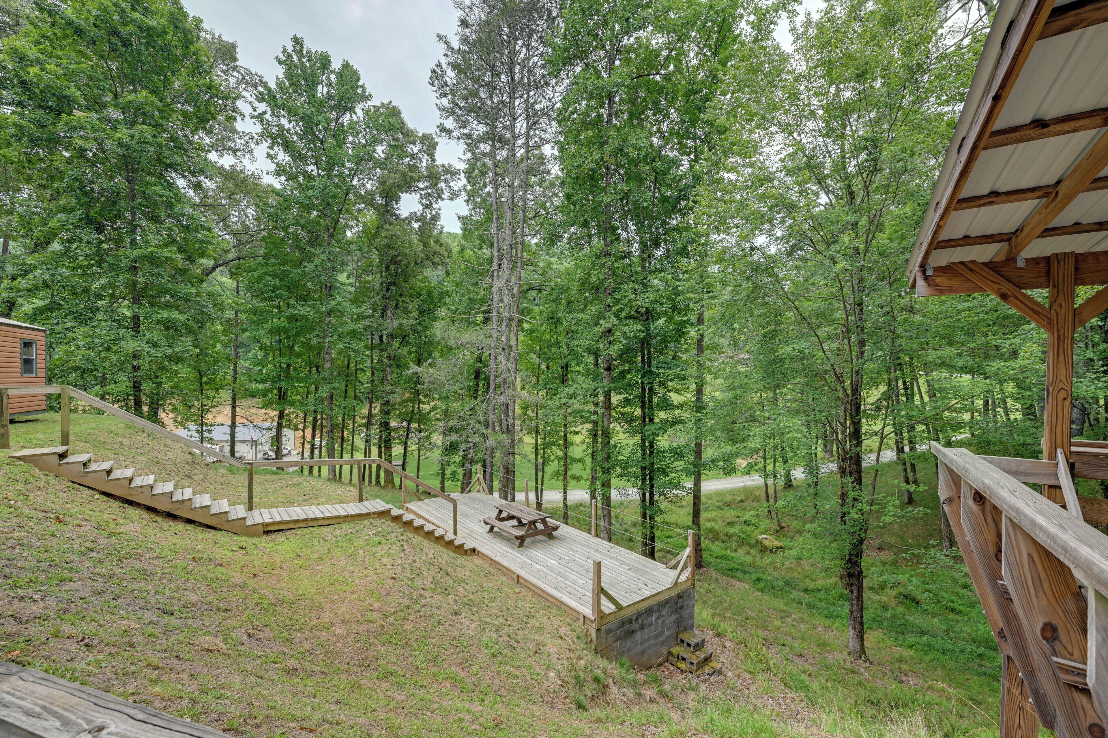 Eine Holzterrasse mit Picknicktisch, umgeben von bewaldeter Landschaft, im Hintergrund eine kleine Holzhütte.