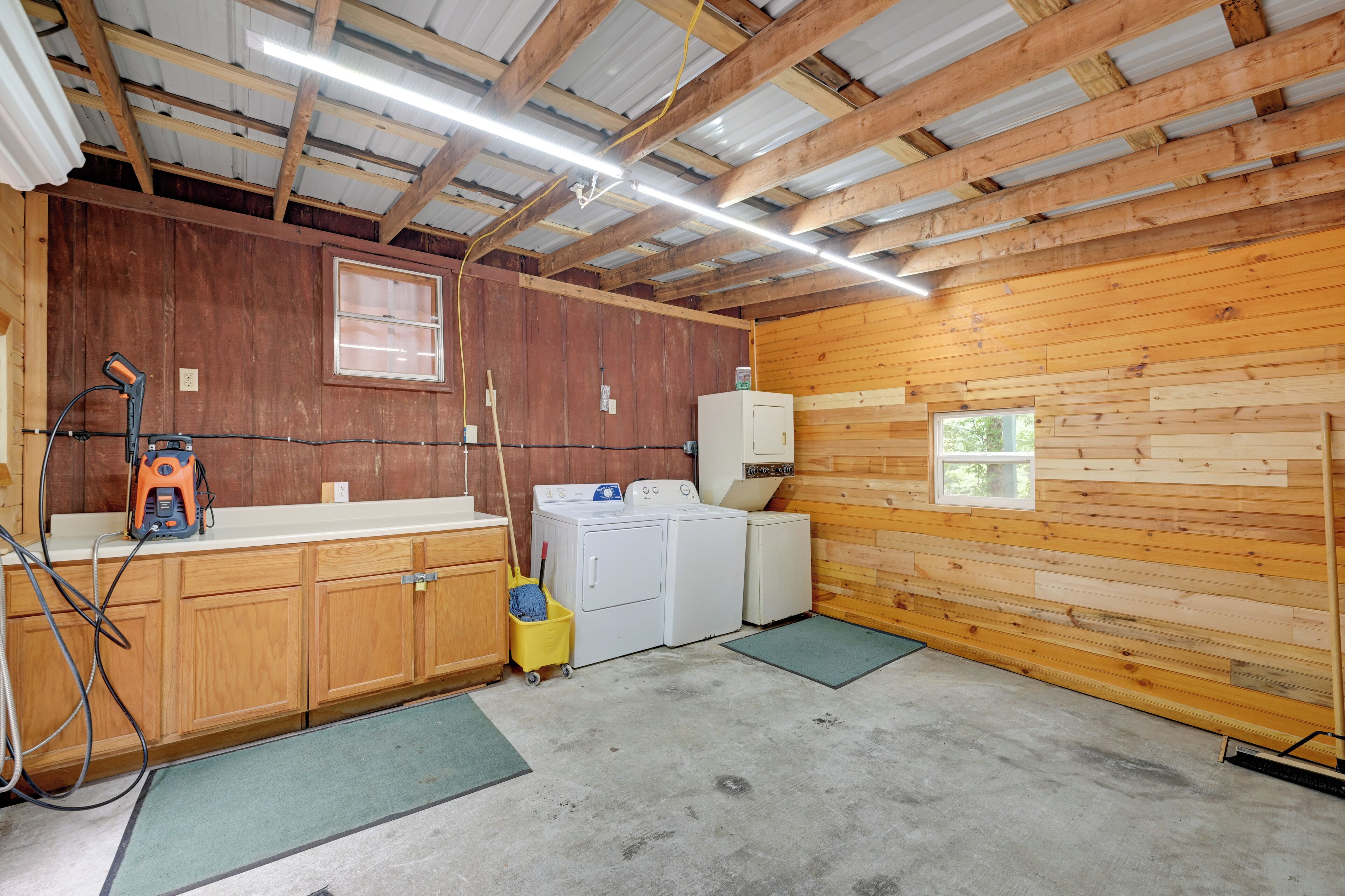 A laundry room with wooden walls, a washing machine, a dryer, and a utility sink.