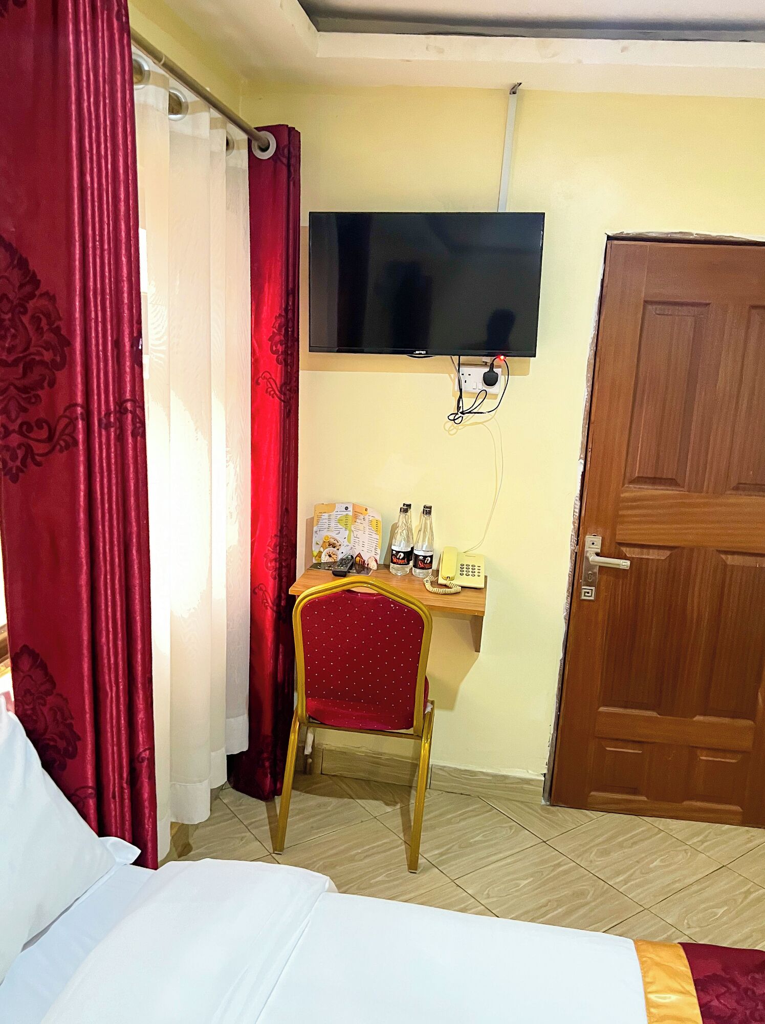 Une chambre d’hôtel comprenant un lit, un bureau avec une chaise, un téléviseur fixé au mur et une porte en bois.