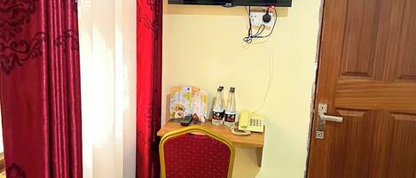 A hotel room with a bed, a desk with a chair, a television mounted on the wall, and a wooden door.