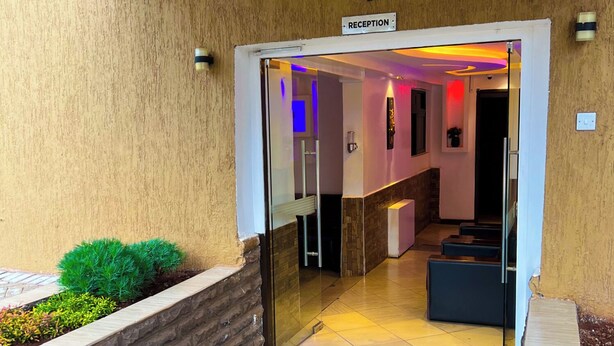 A reception area with a sign, a glass door, a small garden, and a tiled floor. - Sky Park Lounge (Nairobi)