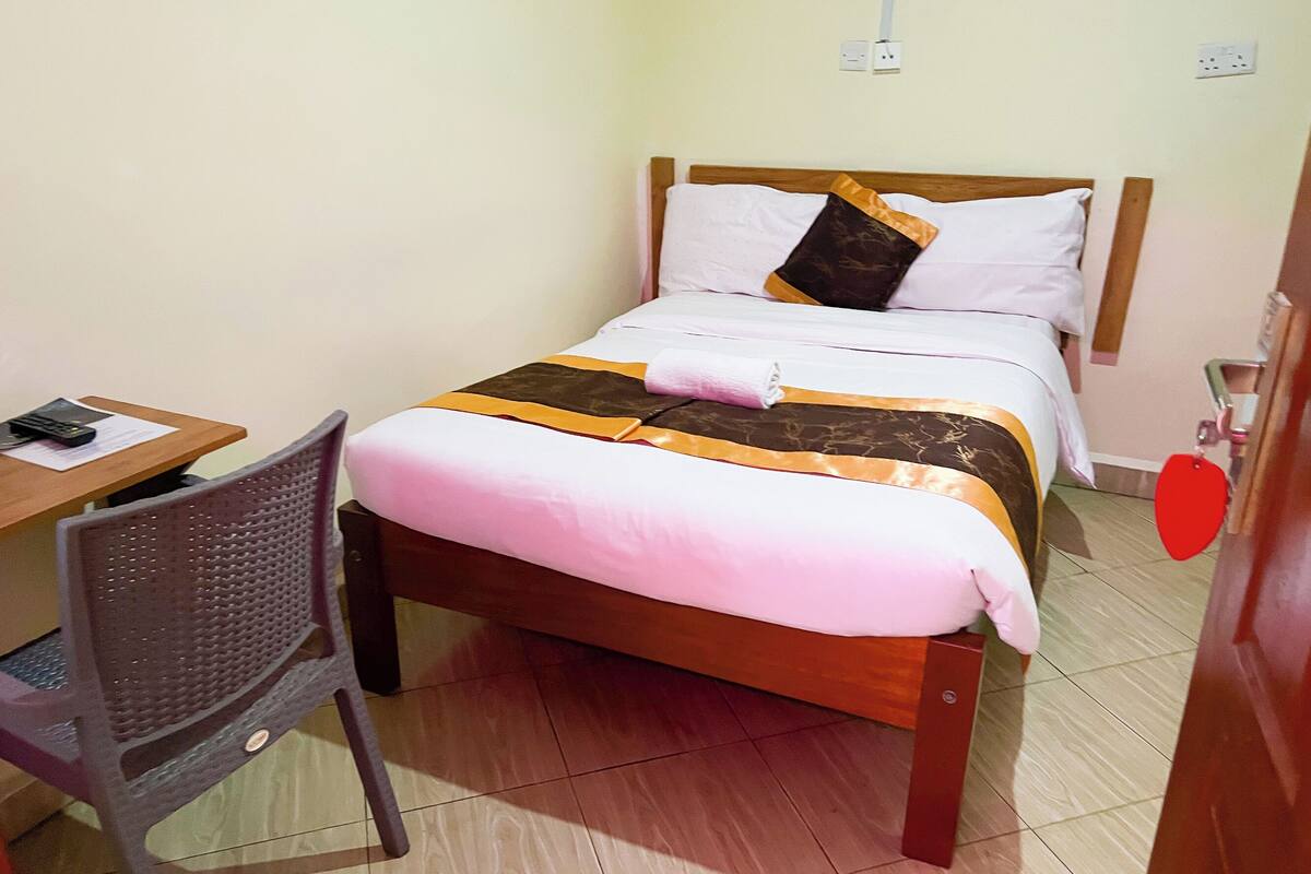 A single bed with a wooden frame, a desk with a chair, and a red heart-shaped decoration on the wall.