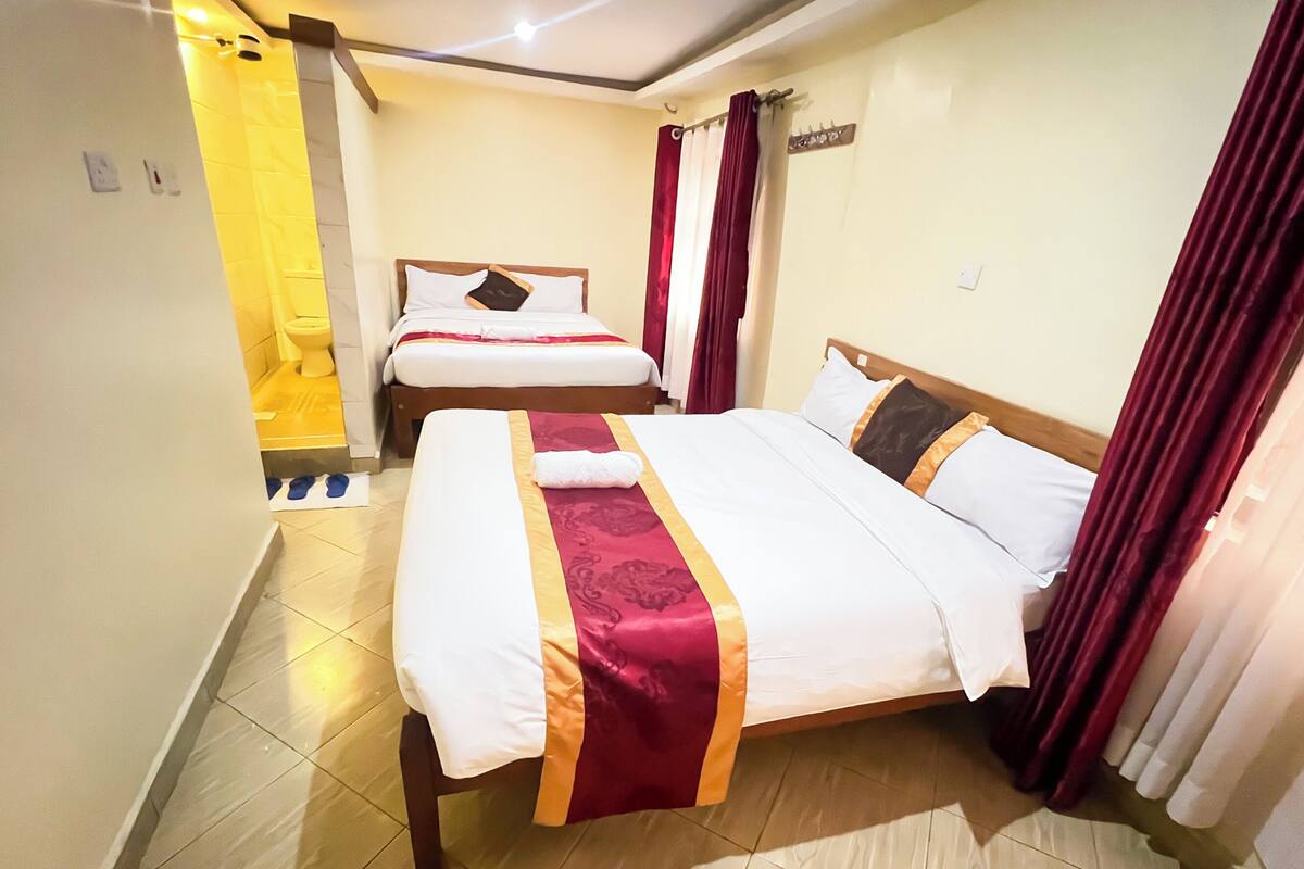 A hotel room with two beds, a bathroom, and a shower area.