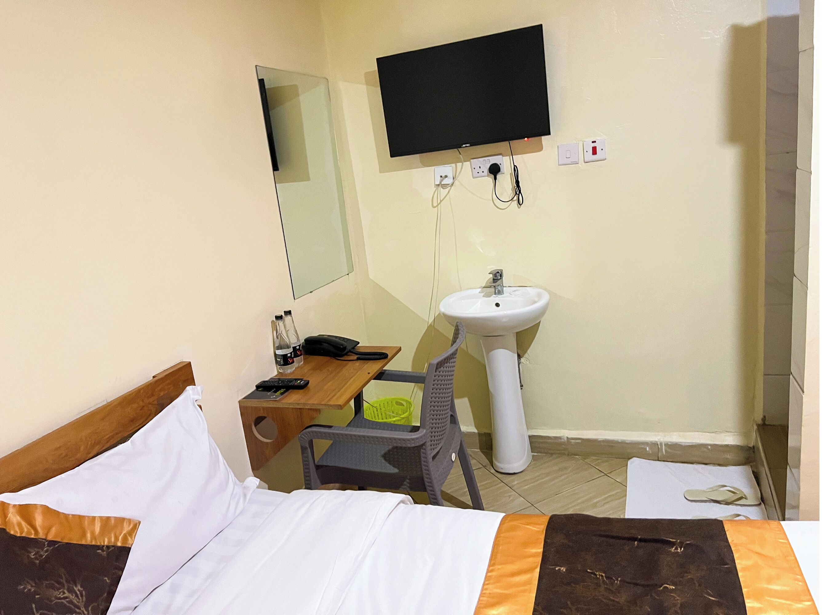 A hotel room with a bed, a desk with a telephone, a sink, and a television mounted on the wall.