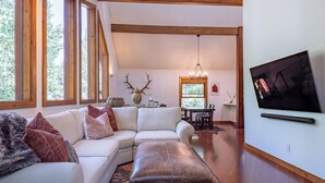 Un salon moderne avec un canapé d’angle blanc, un pouf en cuir et un grand téléviseur à écran plat fixé au mur.