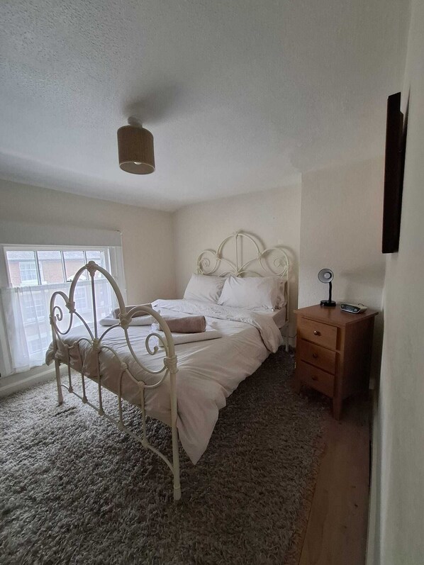 A bedroom with a metal bed frame, a wooden nightstand, a small table, and a window with blinds. - Georgian House to let in Newtown, Powys. Mid Wales.
Accommodation for 4 persons. (Newtown)
