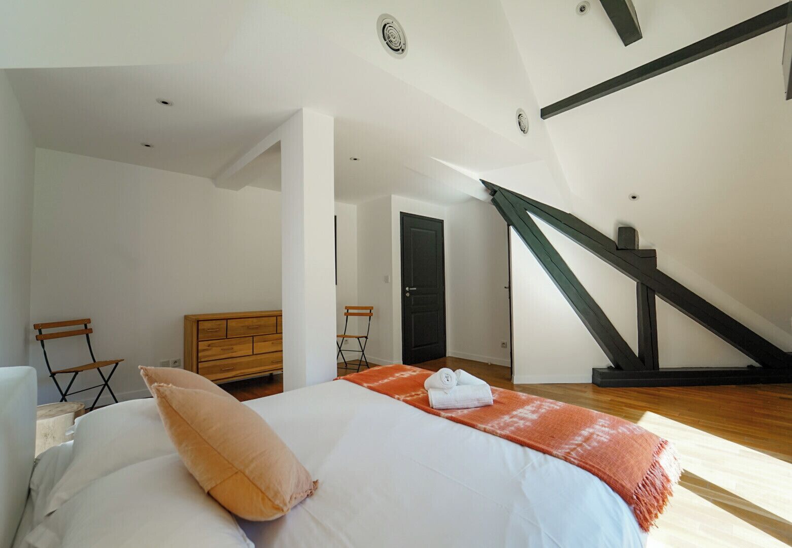 A bedroom with a bed, a wooden dresser, a chair, and a staircase.