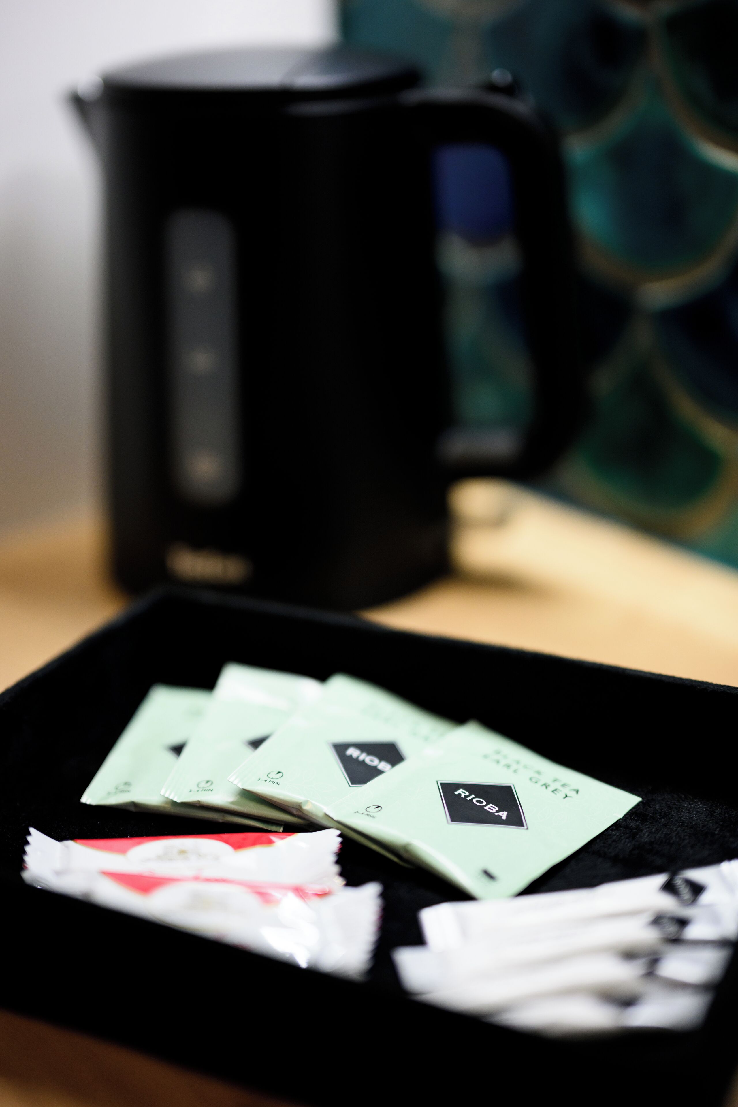 A black coffee maker on a table with a tray containing several packets of coffee and a white cloth.