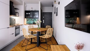A modern kitchen with a dining area, featuring a round wooden table, wicker chairs, and a black door. - Native Apartments Barska 69 (Kraków)