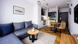 A modern living room with a grey sofa, a wooden coffee table, and a dining area with wicker chairs and a wooden table. - Native Apartments Barska 69 (Kraków)