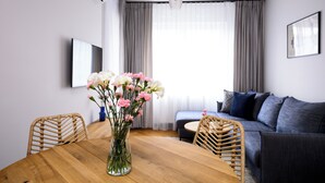 A modern living room with a wooden dining table, wicker chairs, a sofa, and a large window with curtains. - Native Apartments Barska 69 (Kraków)