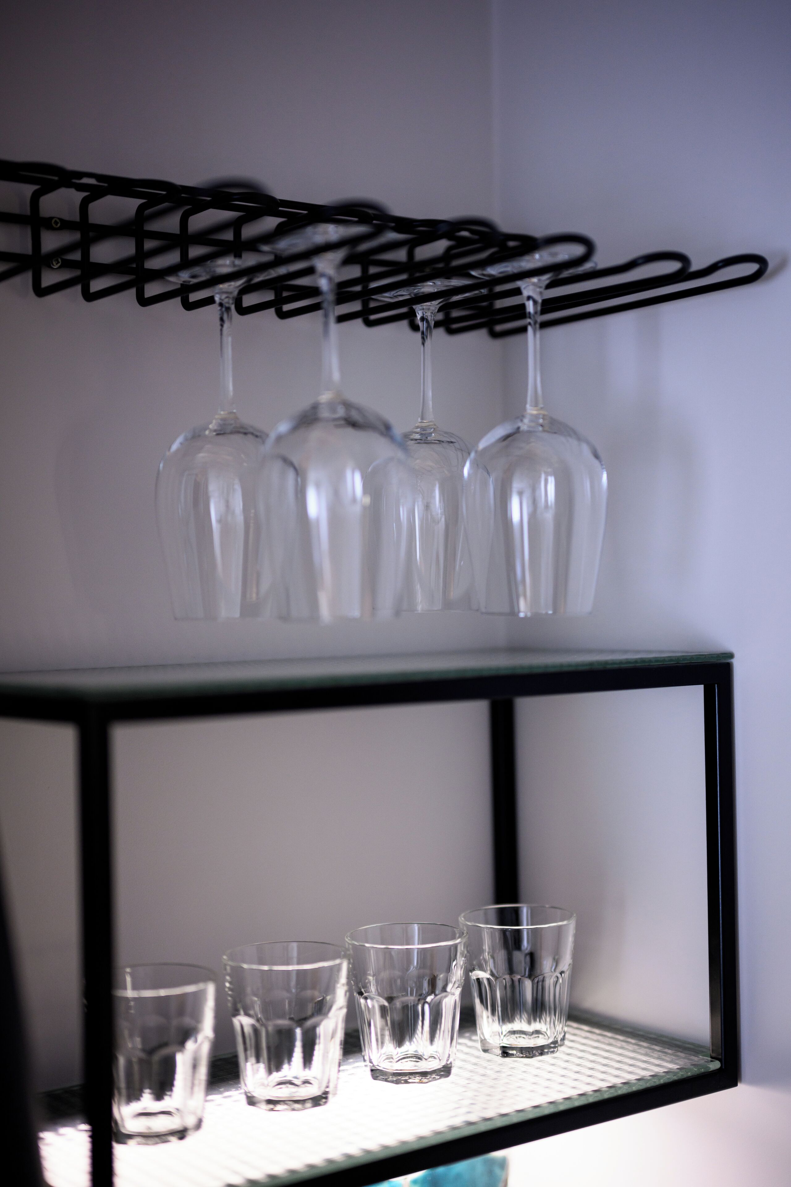 A black metal shelf with four wine glasses hanging above and five wine glasses on the shelf below.