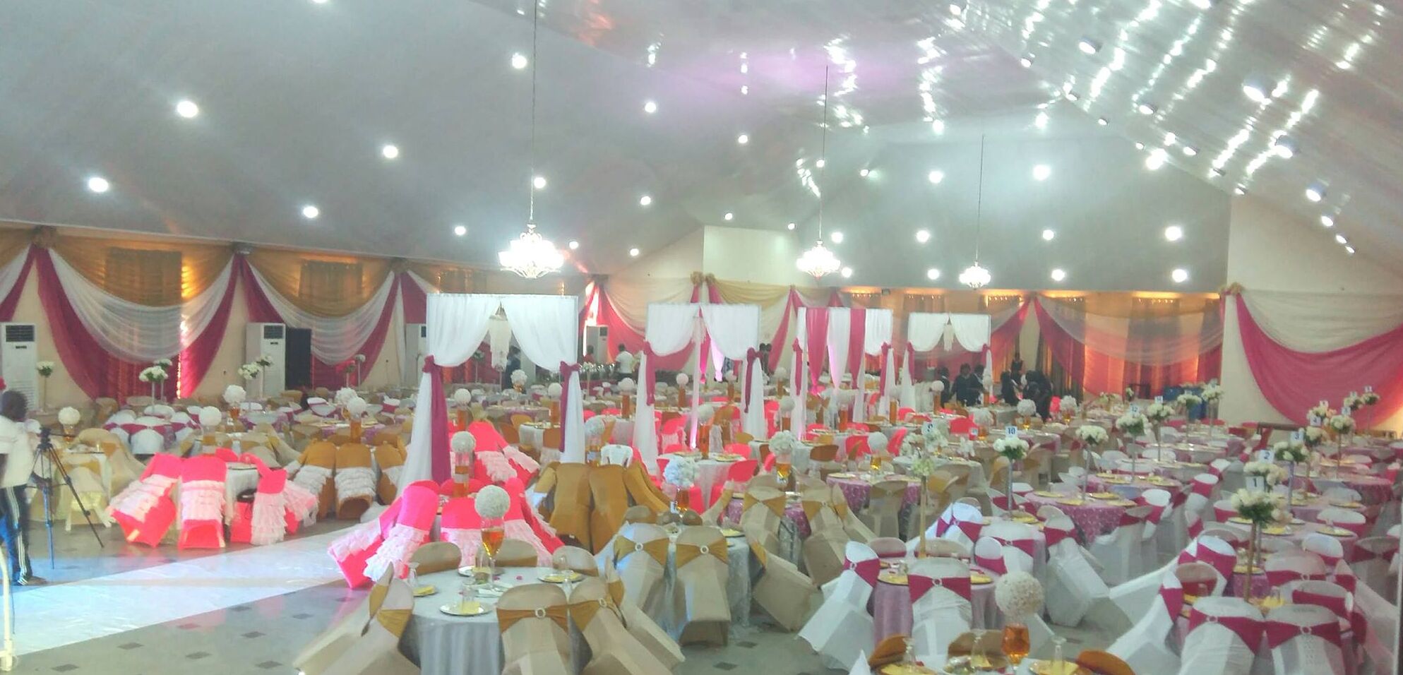 A large indoor event space with multiple round tables, each with white tablecloths and gold sashes.