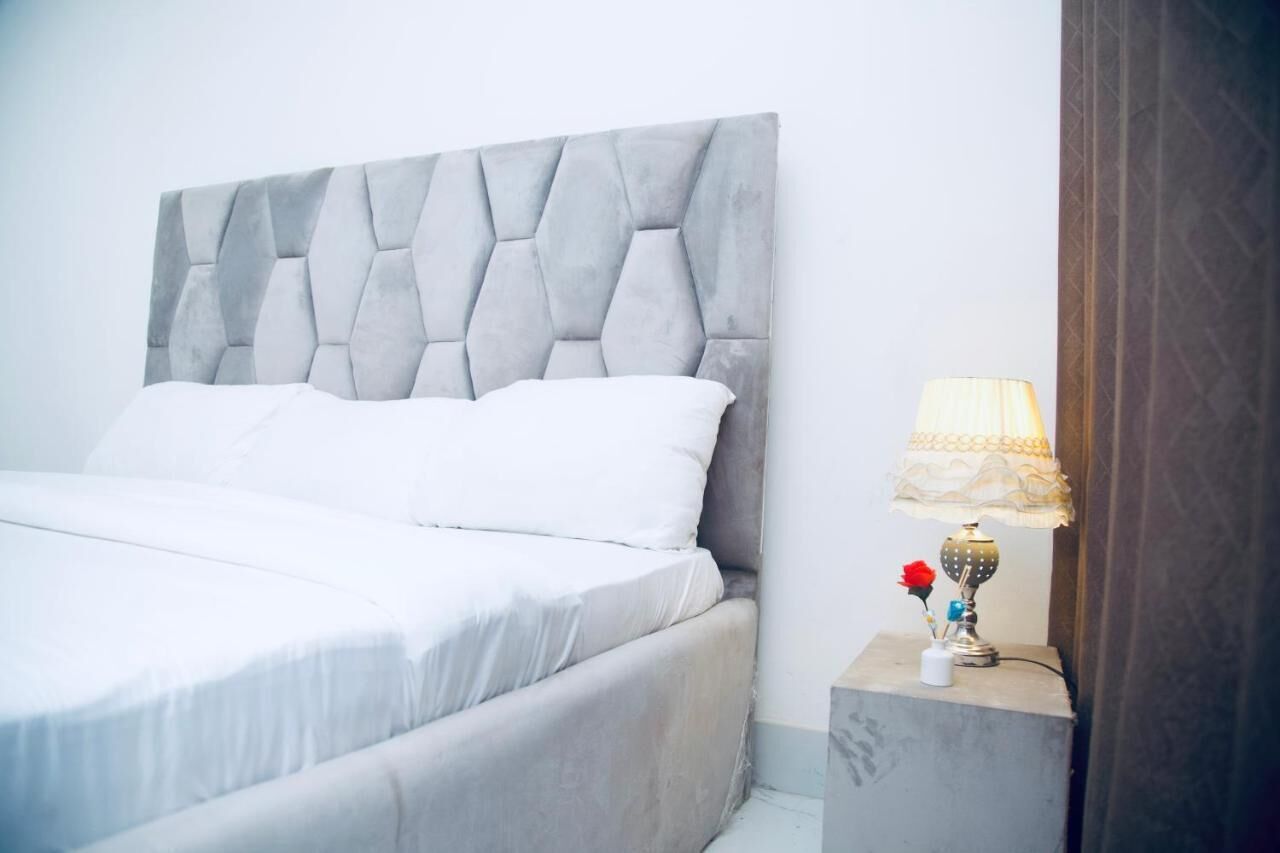 A bed with a tufted headboard, white bedding, and a bedside table with a lamp and a small vase with a flower.
