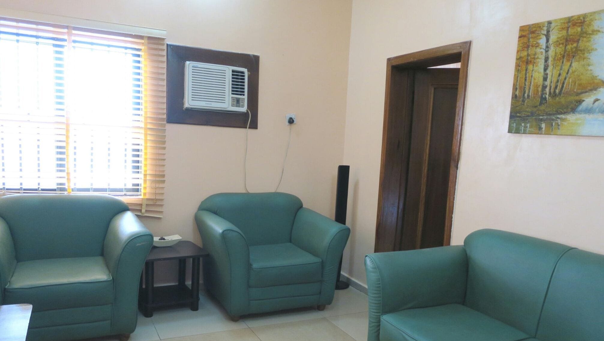 A room with two green armchairs, a small table, and a painting on the wall.
