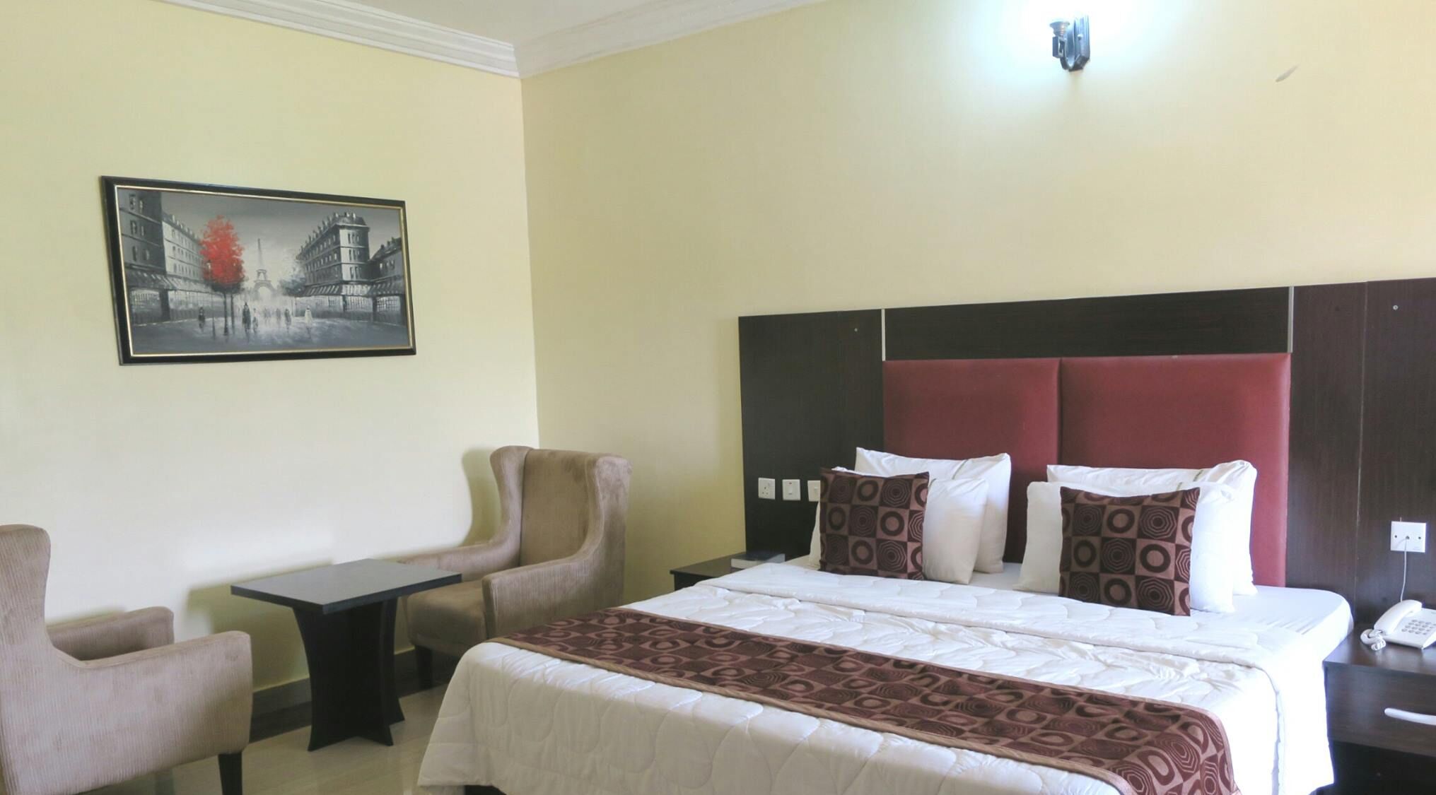 A hotel room with a bed, a desk, a chair, and a painting on the wall.