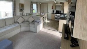 Una sala moderna con un sofá modular, un pequeño espacio de cocina y una mesa de comedor.