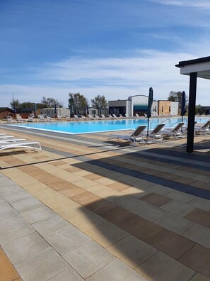 Une piscine entourée de bâtiments et d’arbres, avec des chaises longues et des parasols.