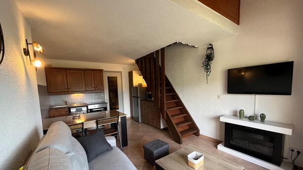 A modern living room with a sofa, a coffee table, and a fireplace. There is a kitchen area with cabinets and a TV mounted on the wall. - T2 Apartment in Quiet Area Near Slopes, Corrençon-en-Vercors (Corrençon-en-Vercors)