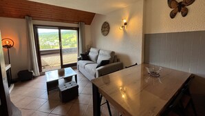 A cozy living room with a sofa, a dining table, and a view through a sliding glass door. - T2 Apartment in Quiet Area Near Slopes, Corrençon-en-Vercors (Corrençon-en-Vercors)