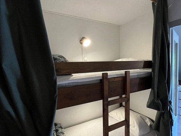 Een stapelbed met bureau en stoel, een bedlampje en een raam met gordijnen.