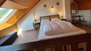 A bedroom with a sloped ceiling, a bed with white bedding, two bedside tables with lamps, a chair, and a window with a view of greenery. - T2 Apartment in Quiet Area Near Slopes, Corrençon-en-Vercors (Corrençon-en-Vercors)