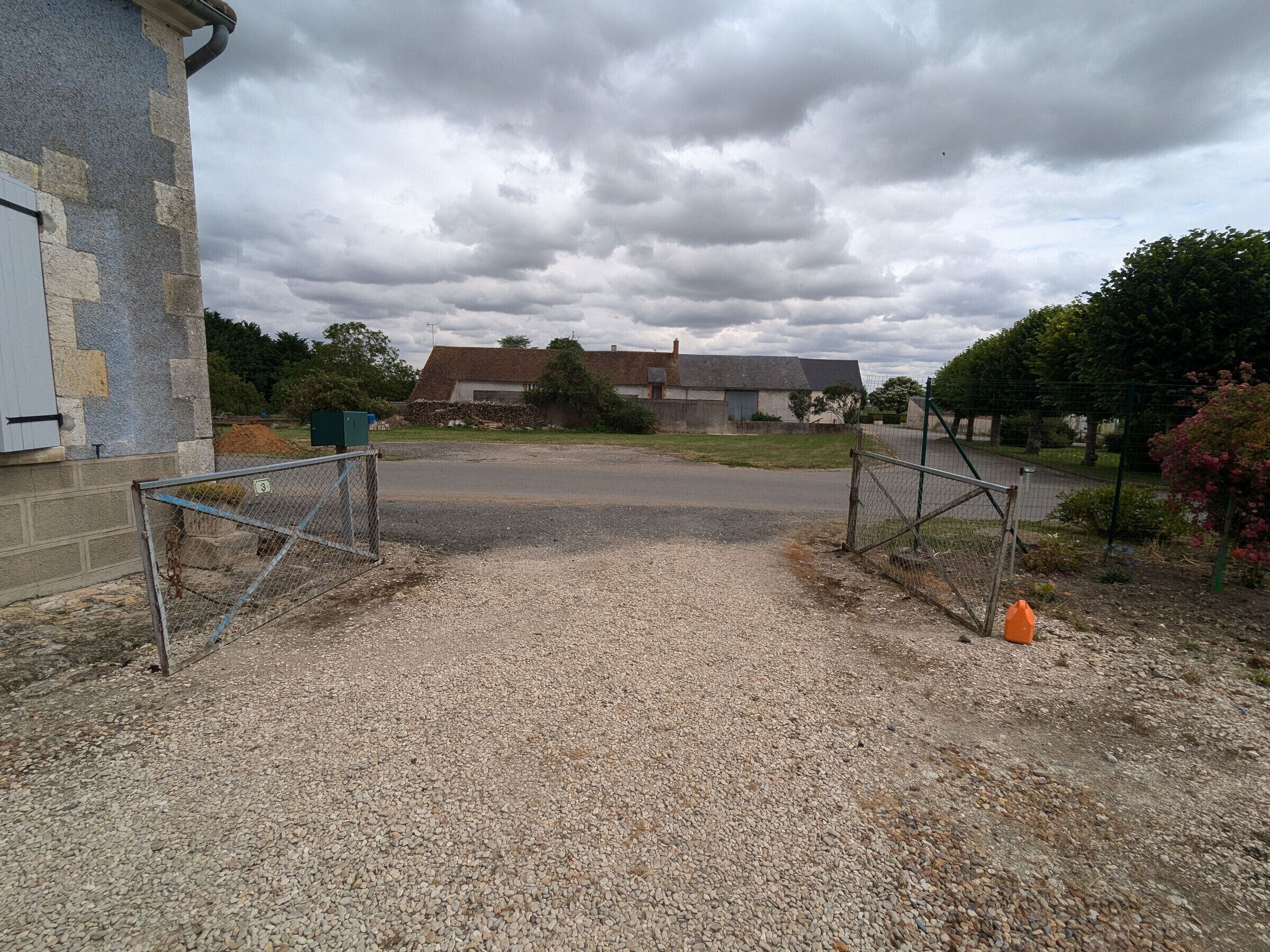 Une allée de gravier mène à une entrée fermée par un portail, avec un bâtiment situé sur la gauche.