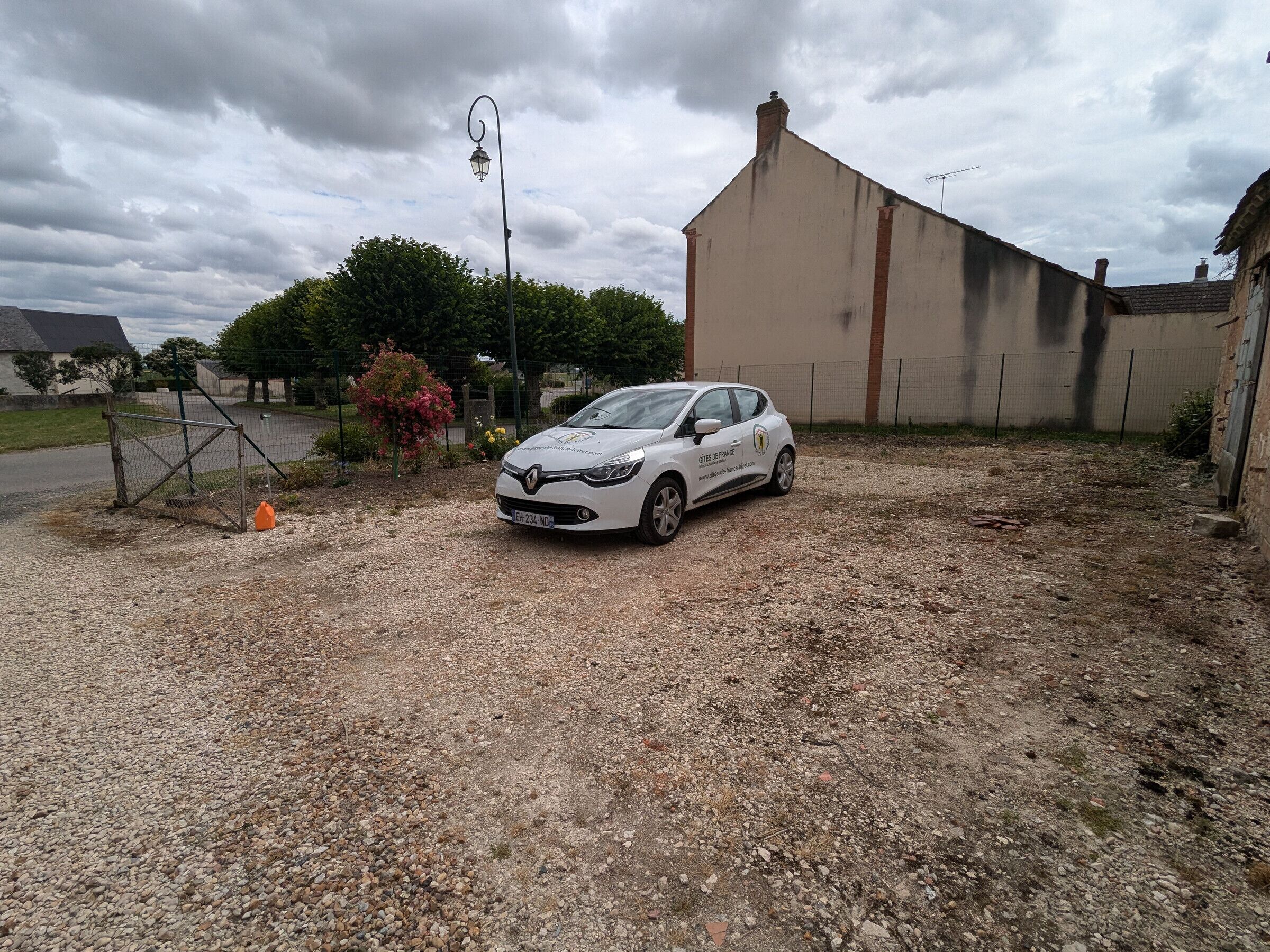 A white car parked in a gravel driveway with a building in the background.