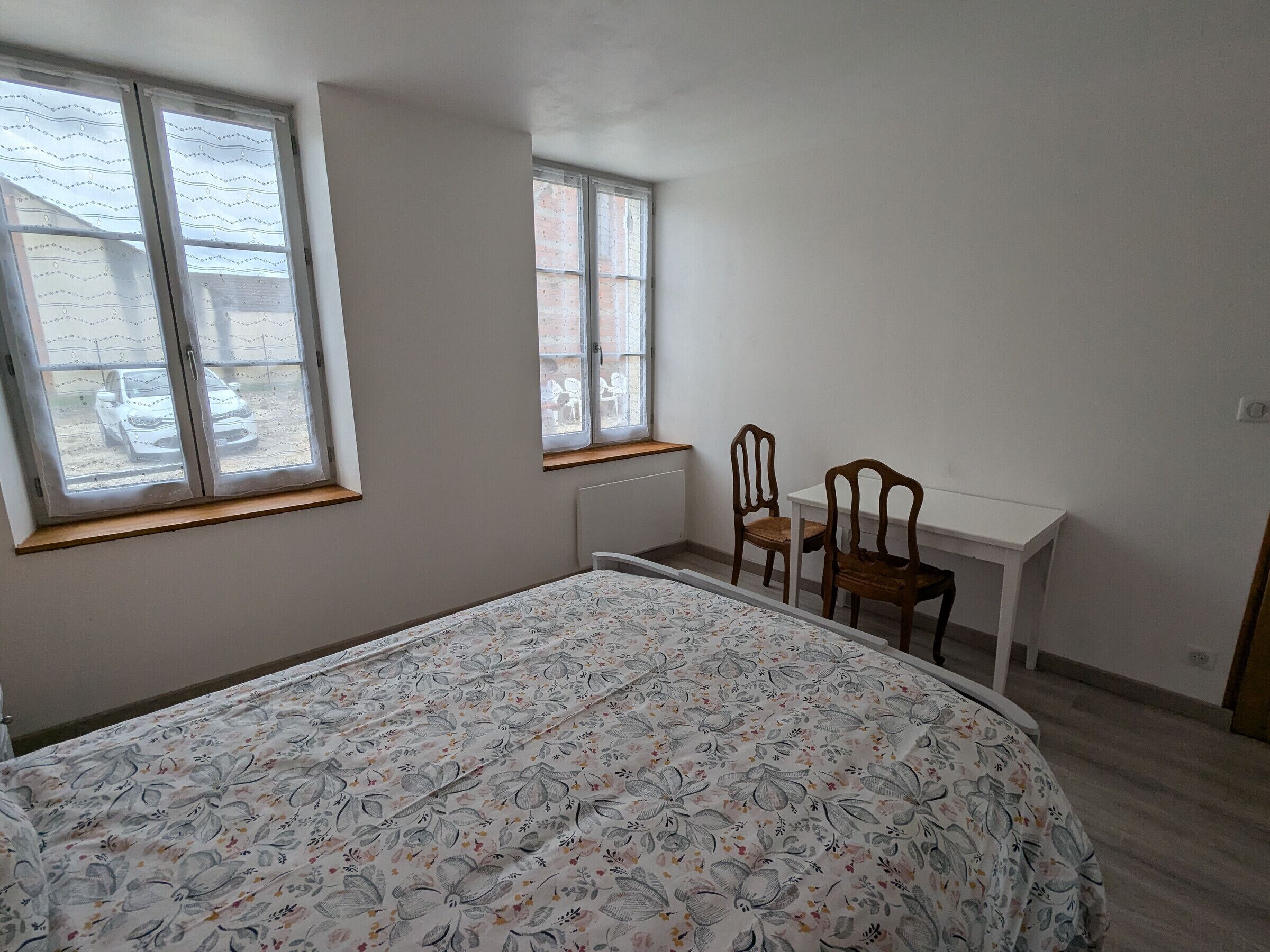 Une chambre à coucher avec un lit, deux fenêtres, un bureau et deux chaises.