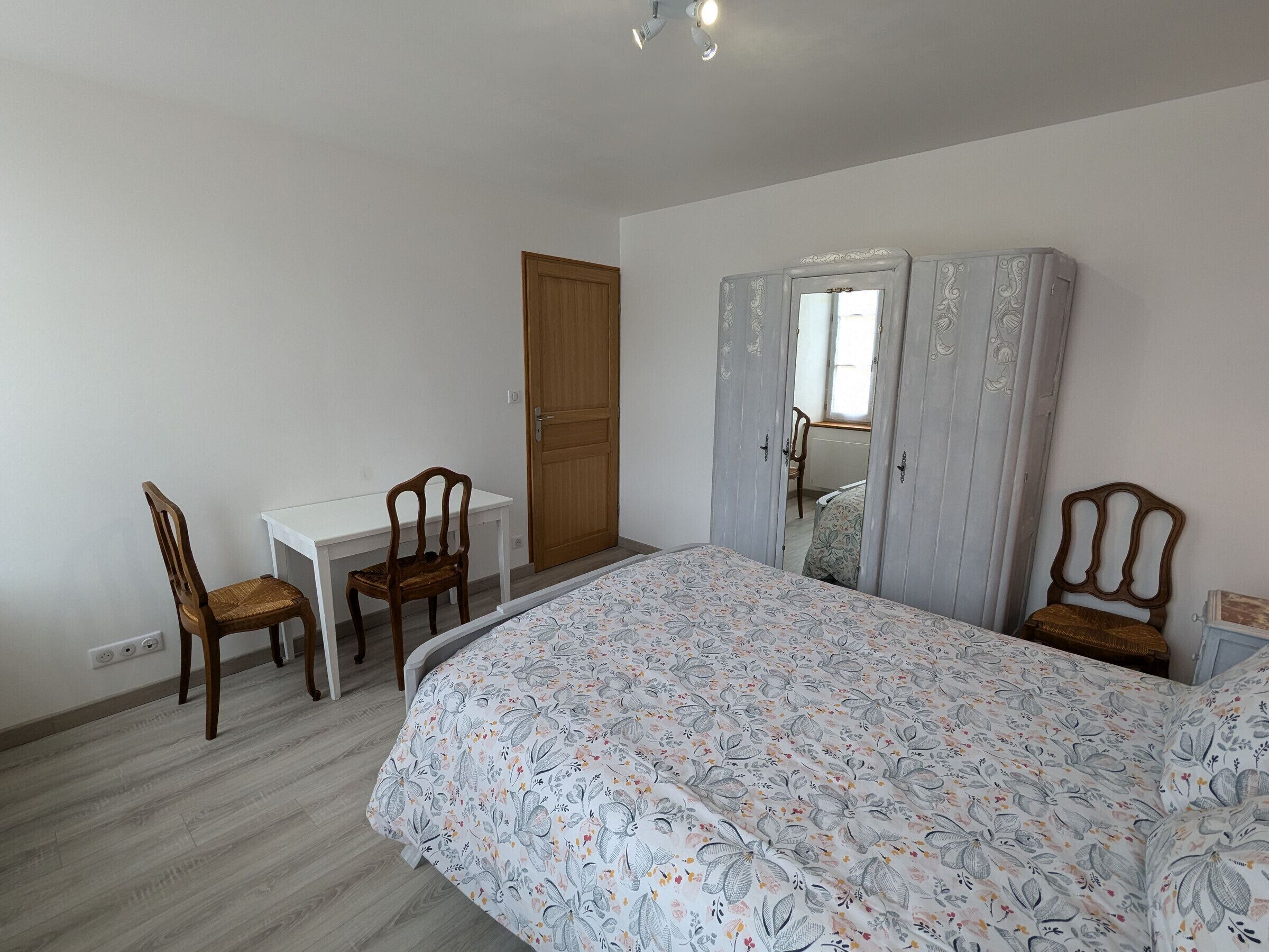 Un dormitorio con cama, escritorio, dos sillas, armario y una puerta.