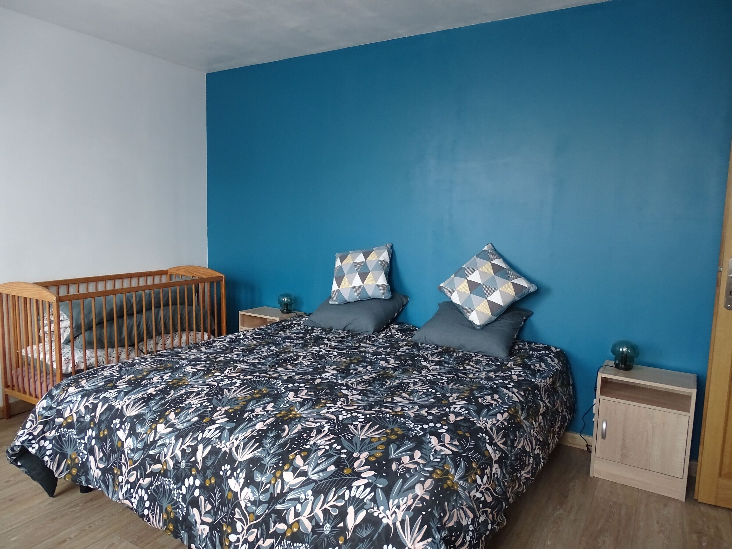 A bedroom with a large bed, a wooden crib, and a blue accent wall.