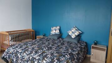 A bedroom with a large bed, a wooden crib, and a blue accent wall.