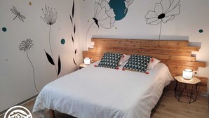 A bedroom with a wooden headboard, white bedding, patterned pillows, and wall decals of flowers and a moon. - Charming cottage in Vendée with spa and sauna (La Roche-sur-Yon)