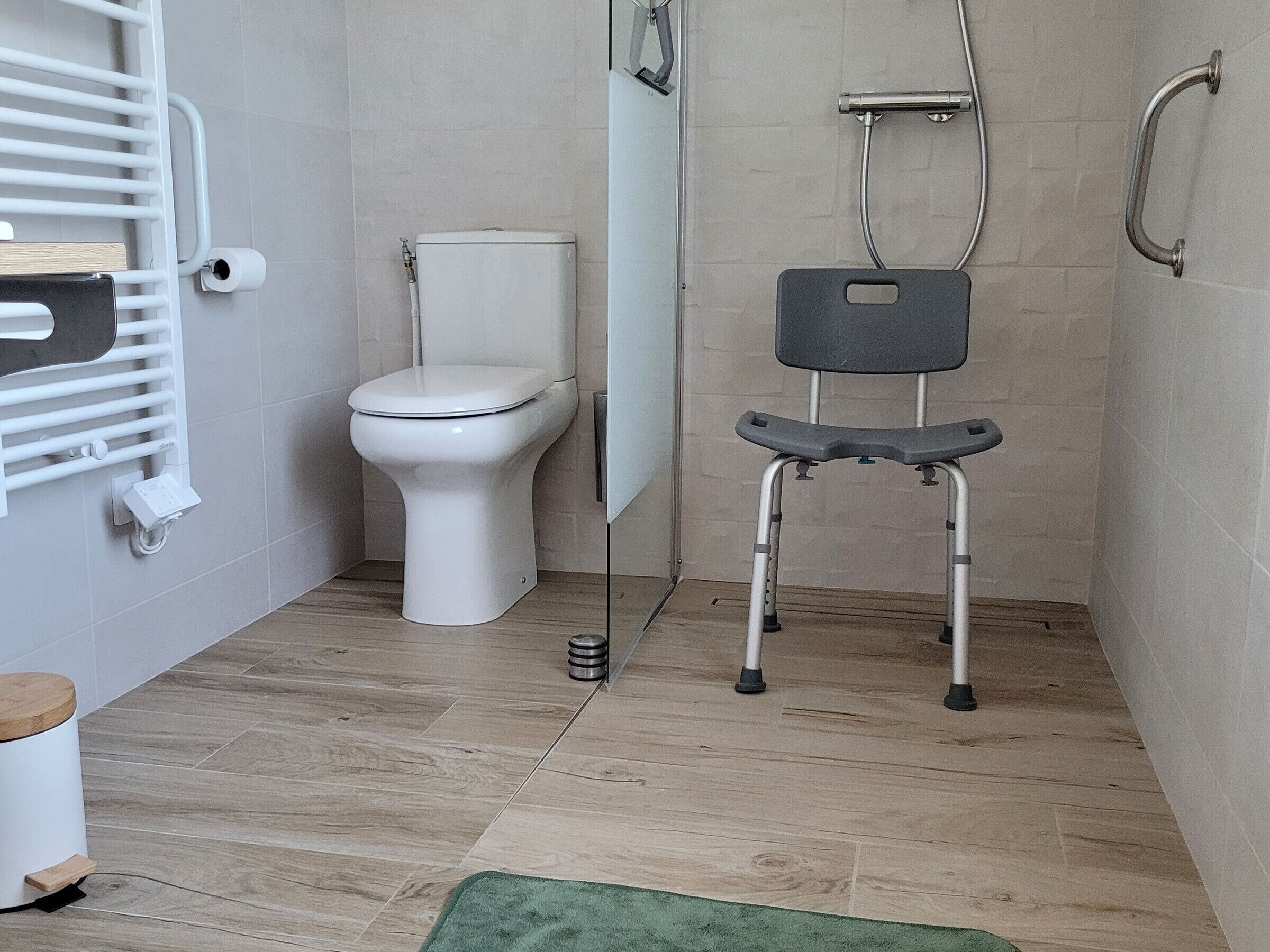 A modern bathroom with a toilet, a shower chair, and a towel rack.
