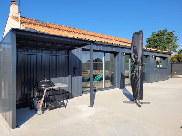 Un bâtiment moderne doté d’un patio couvert, d’un barbecue et d’un grand parasol.