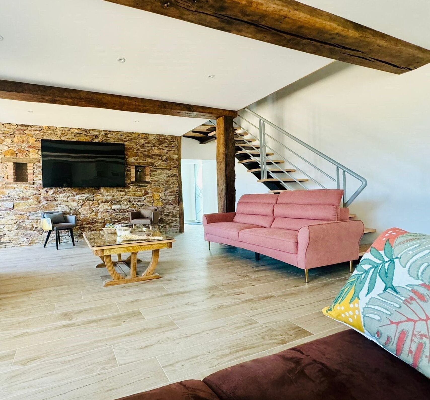A living room with a stone wall, a wooden table, a pink sofa, and a staircase.