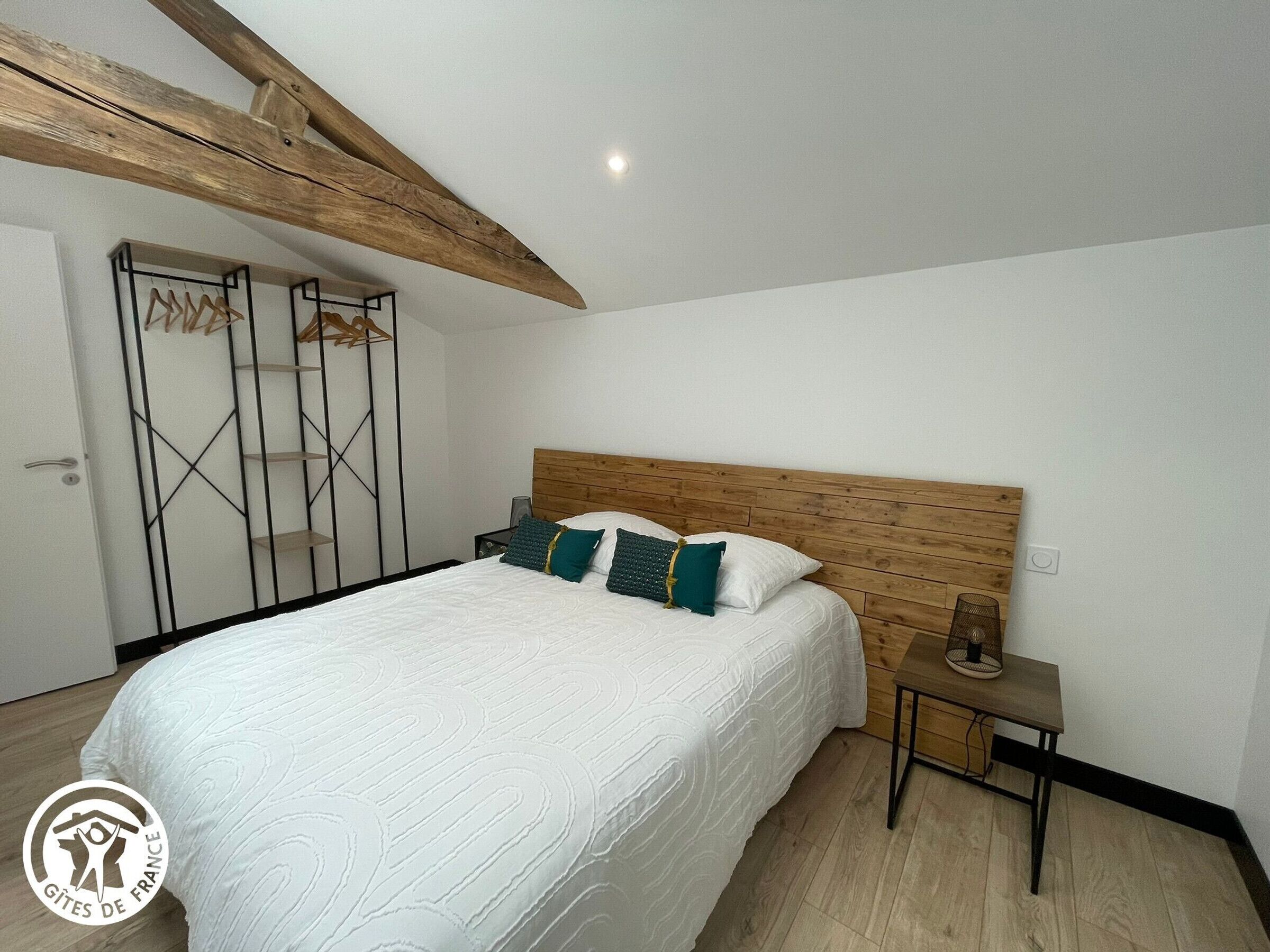 Une chambre à coucher avec une tête de lit en bois, un lit avec une literie blanche, une table de chevet et une étagère fixée au mur.