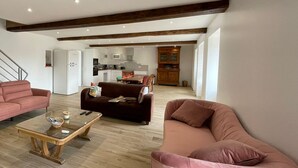 A spacious living area with a wooden floor, a sofa, a coffee table, and a kitchen in the background. - Charming cottage in Vendée with spa and sauna (La Roche-sur-Yon)