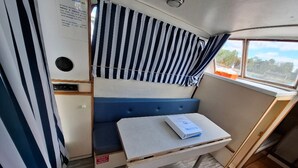 Un intérieur compact et bien éclairé, avec un rideau à rayures, une petite table sur laquelle repose un livre et un banc.