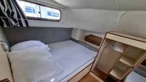Une petite cabine bien éclairée, équipée d’un lit simple, d’une petite étagère en bois et d’une fenêtre donnant sur un paysage agréable.