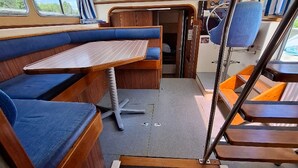 Ein schmaler Bootsinnenraum mit Holzsitzgelegenheiten, einem kleinen Tisch und einem Bullaugenfenster.